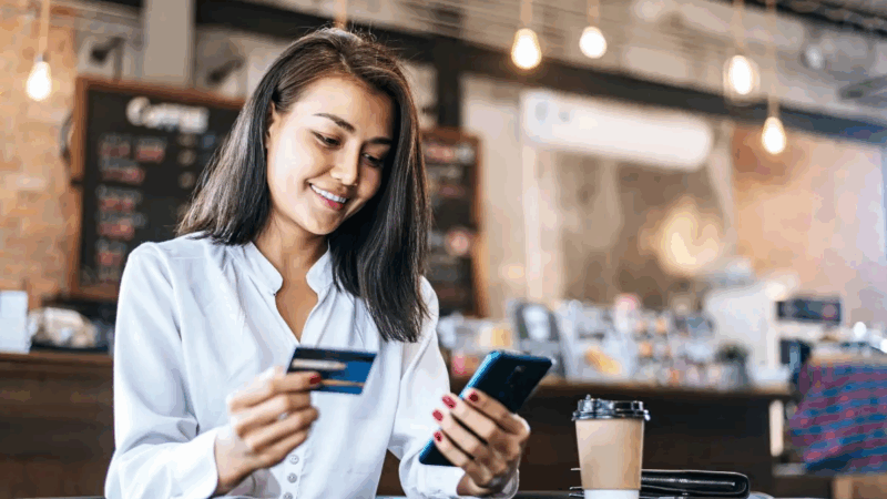 Junge Frau nutzt Smartphone und Kreditkarte für Online-Einkauf in einem Café
