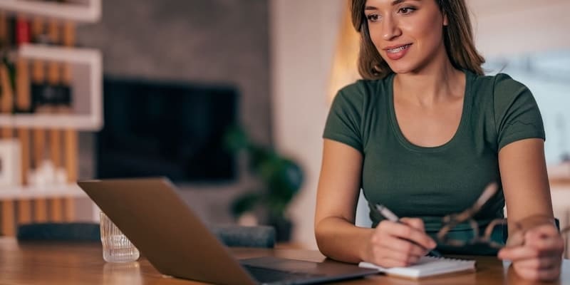 Frau recherchiert am Laptop über Auxmoney Erfahrungen und schreibt sich Notizen für ihren Kreditvergleich AB